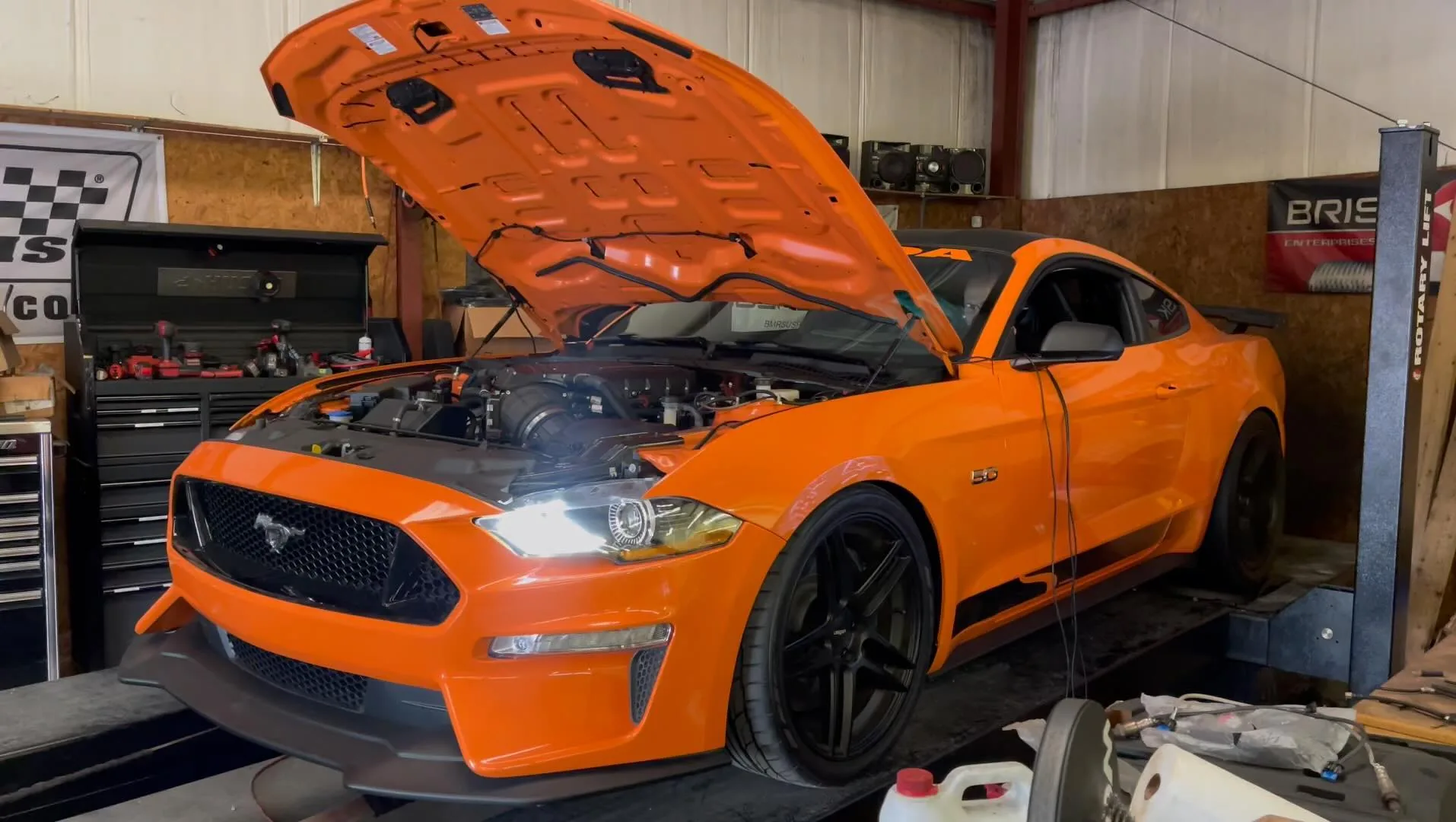 An orange Mustang GT on the dyno with the hood up