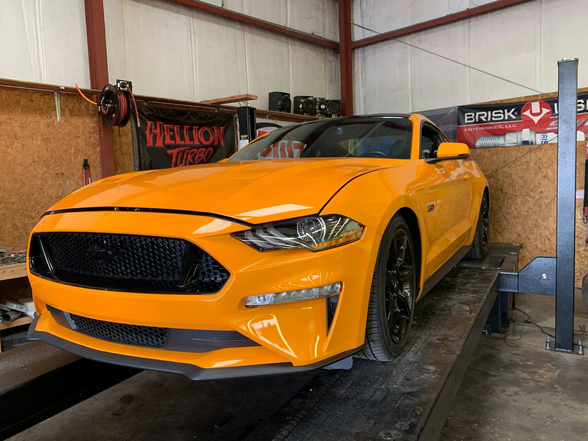 An orange S550 Mustang GT on the lift in the shop