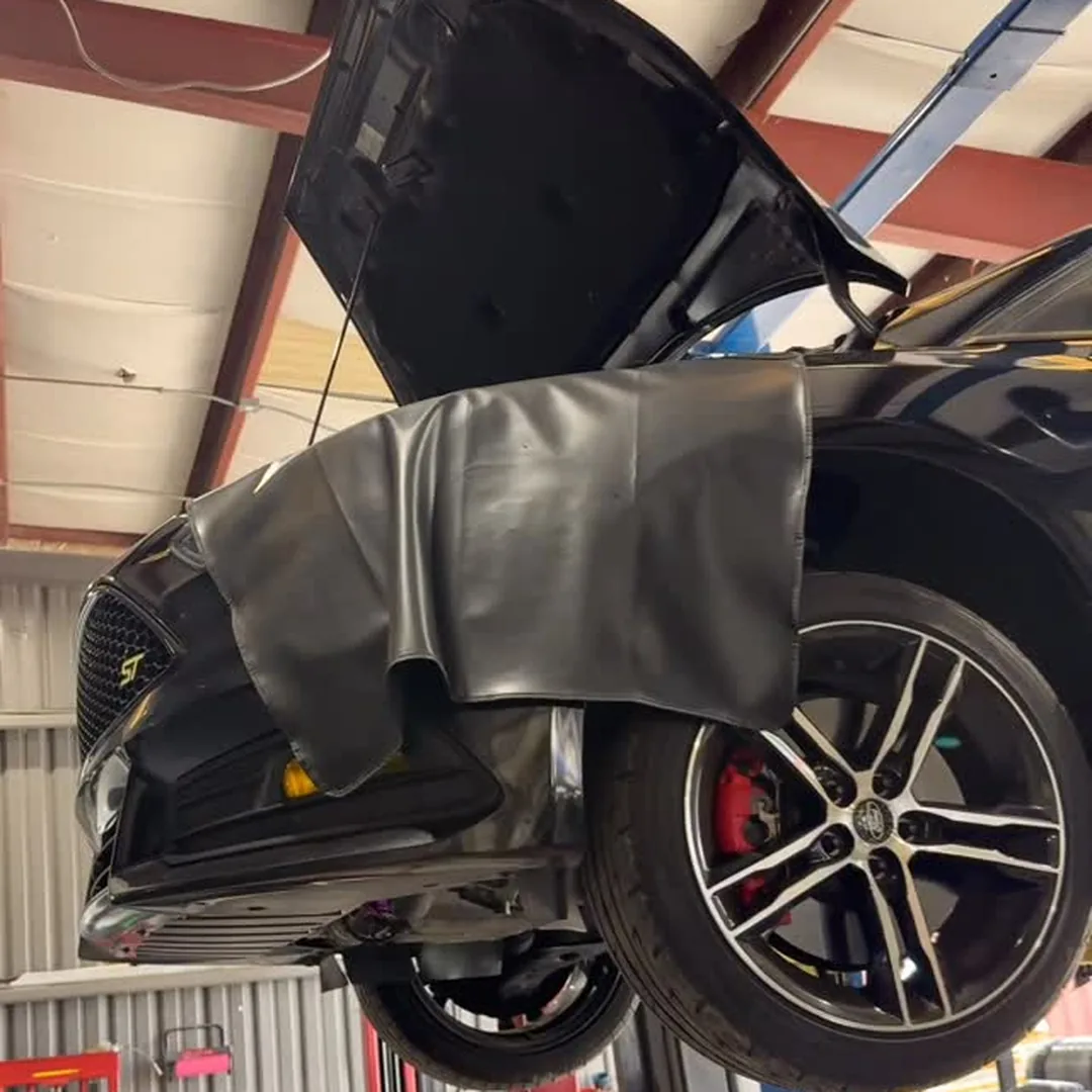 A black Focus ST raised on the lift with the hood open and a fender cover over the wing