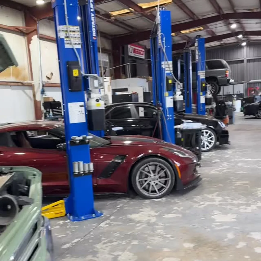 The shop floor with a dark red C7 Corvette on a two post lift and more cars in the bays behind it
