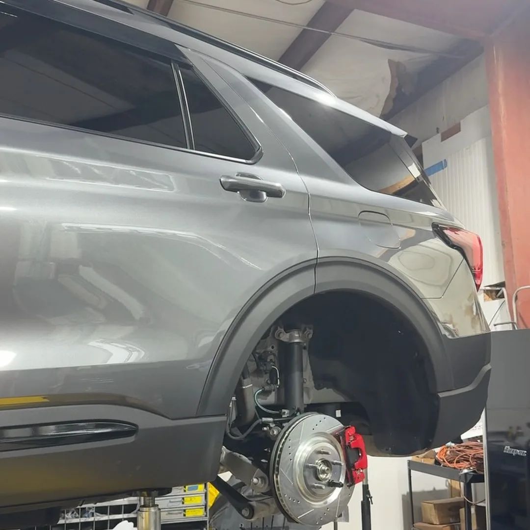 A grey Ford Explorer ST raised on the lift with a rear wheel off, showing a drilled and slotted rotor behind a red caliper