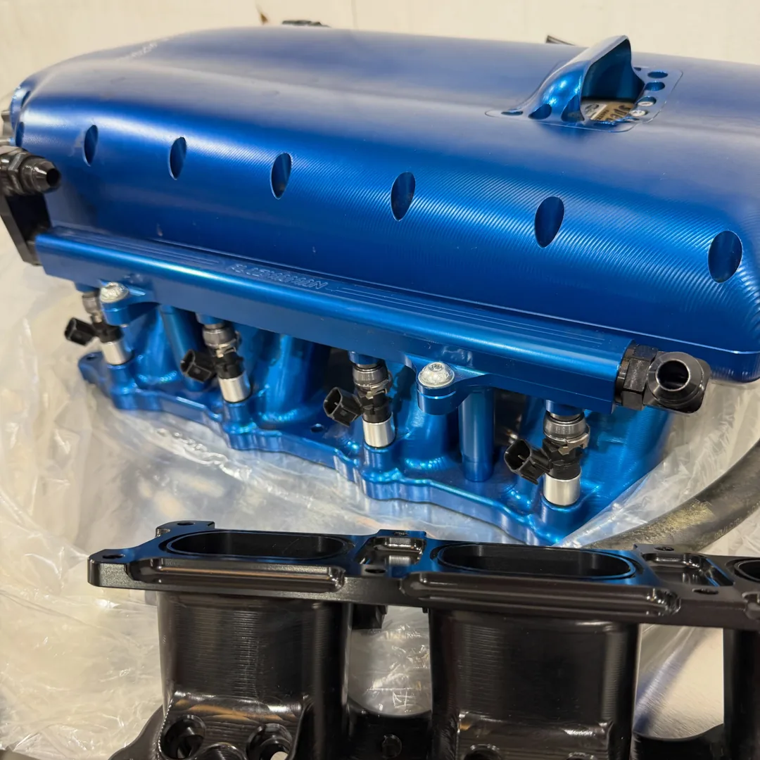 A blue anodized supercharger manifold on the bench, fuel rails and injectors already fitted